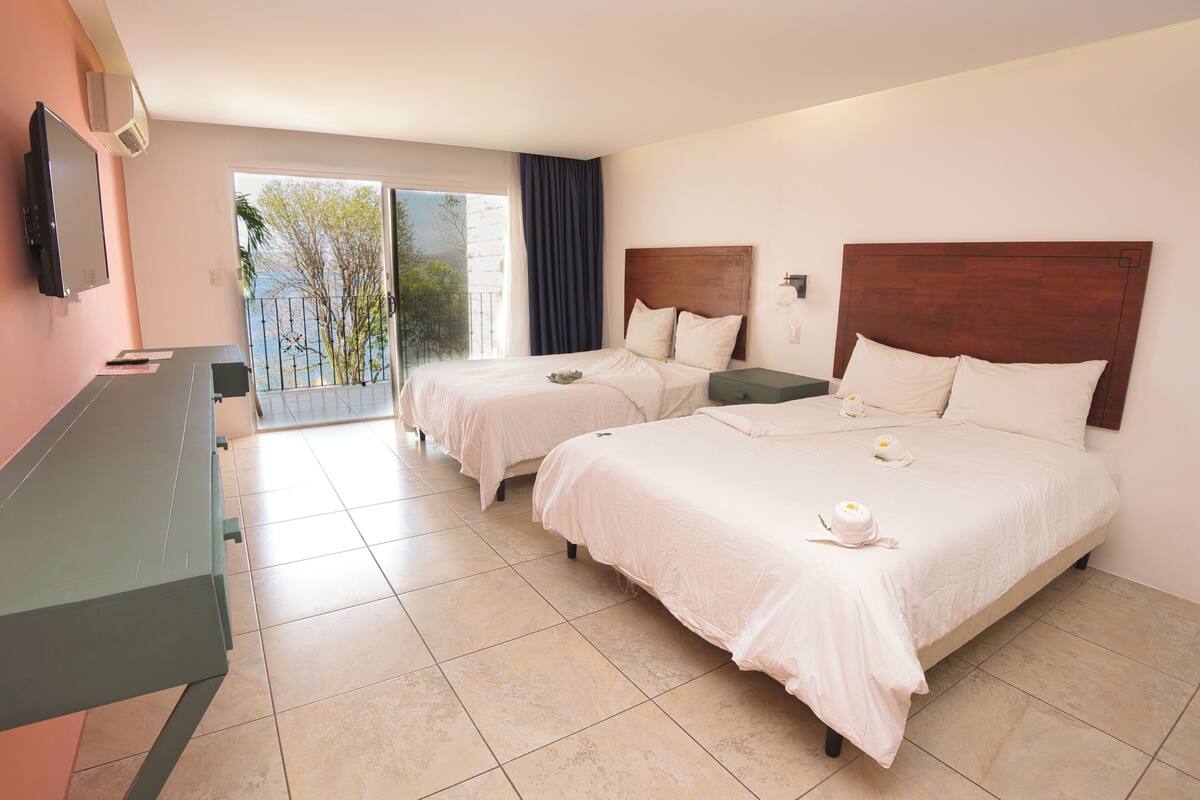 A hotel room with two beds, a TV, and a balcony with a view.