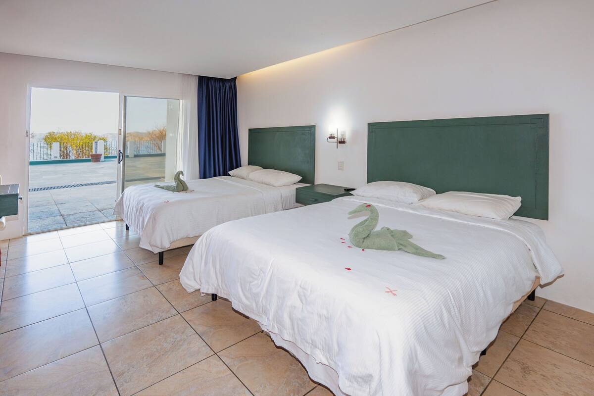 A hotel room with two beds, a large sliding glass door leading to an outdoor area, and a green headboard.
