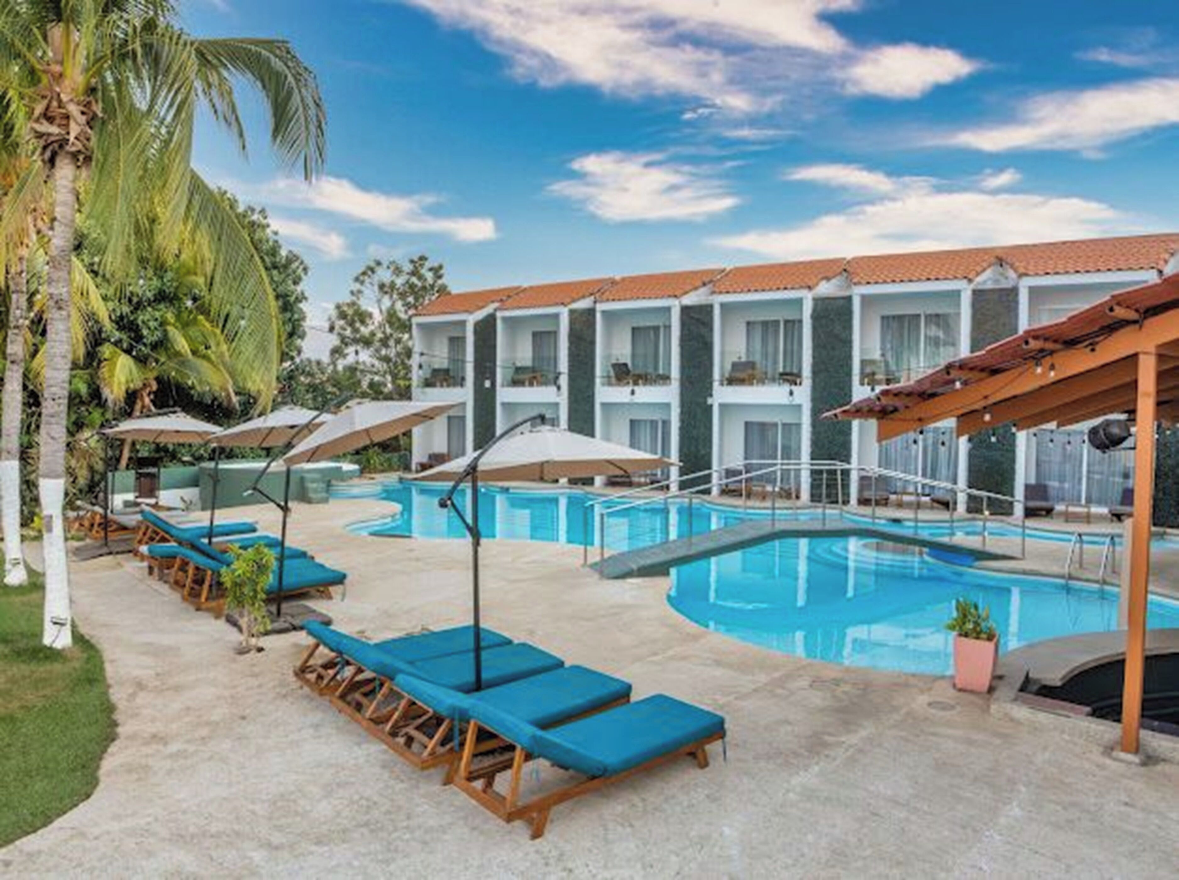 A poolside area with lounge chairs, umbrellas, and a building with balconies in the background.