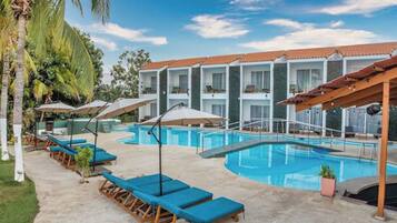 A poolside area with lounge chairs, umbrellas, and a building with balconies in the background.
