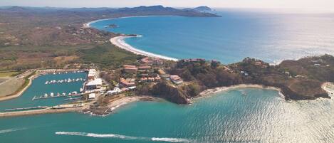 Vista aérea de una zona costera con un puerto deportivo, edificios y una playa.