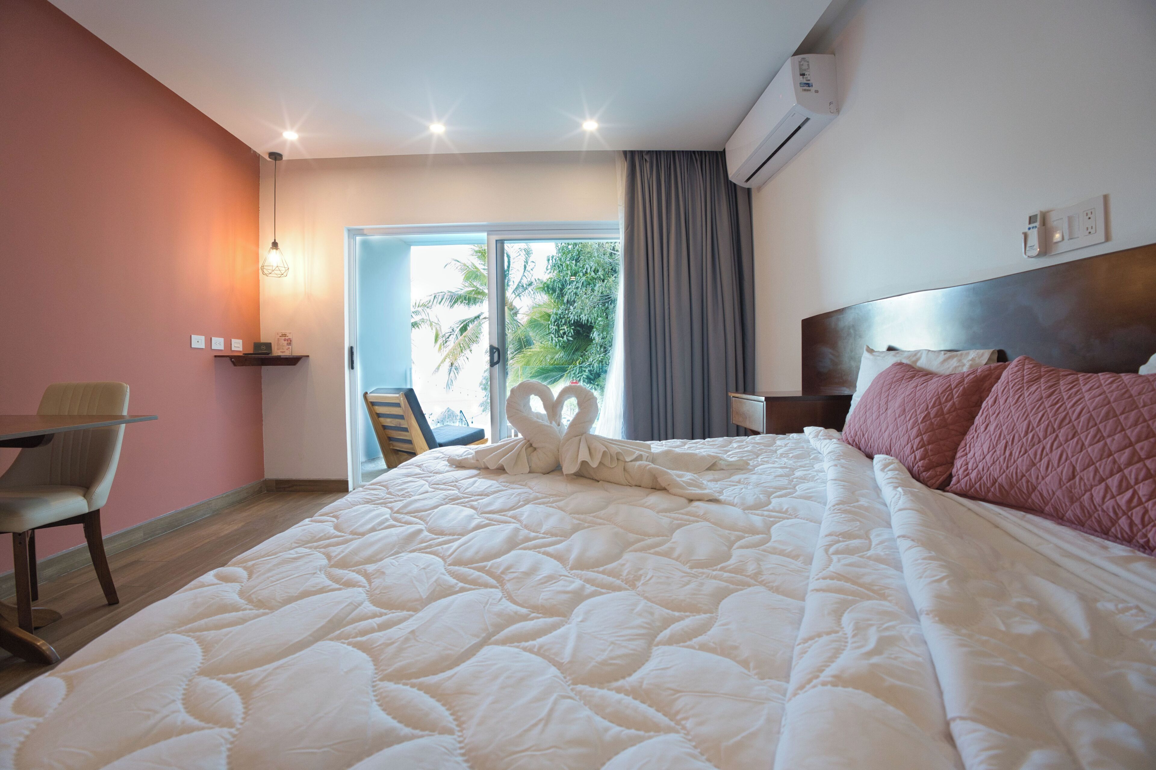 A hotel room with a large bed, a desk, and a view of palm trees through the door.