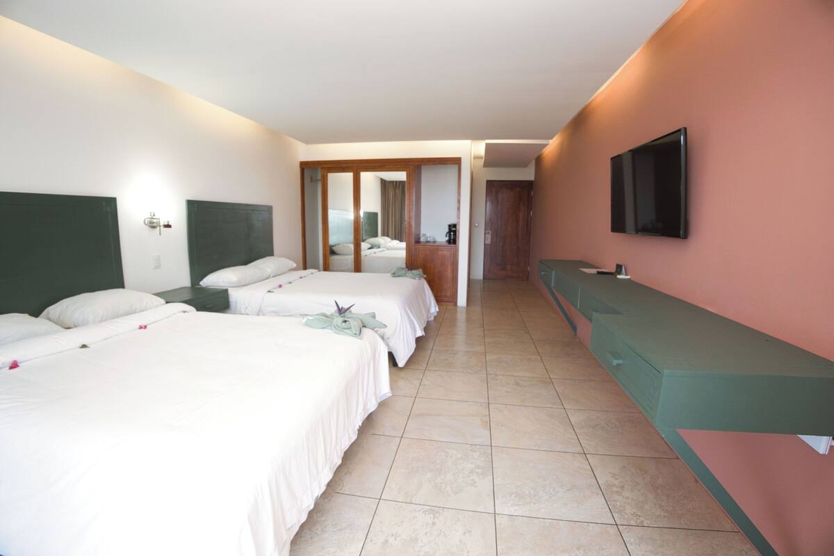 A hotel room with two beds, a bathroom, a TV, and a counter.