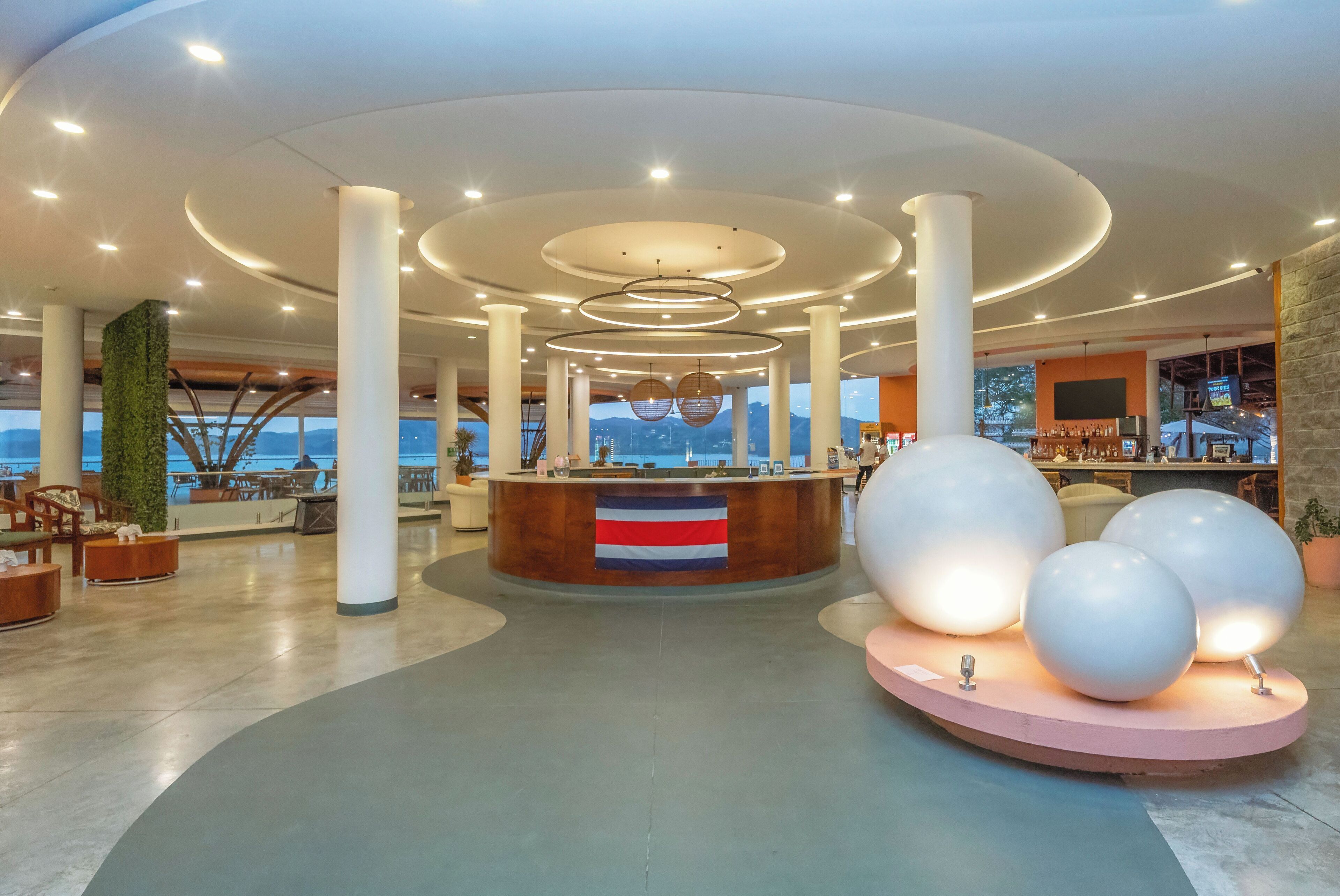 A spacious lobby with a reception desk, large white spherical sculptures, and a view of the sea.