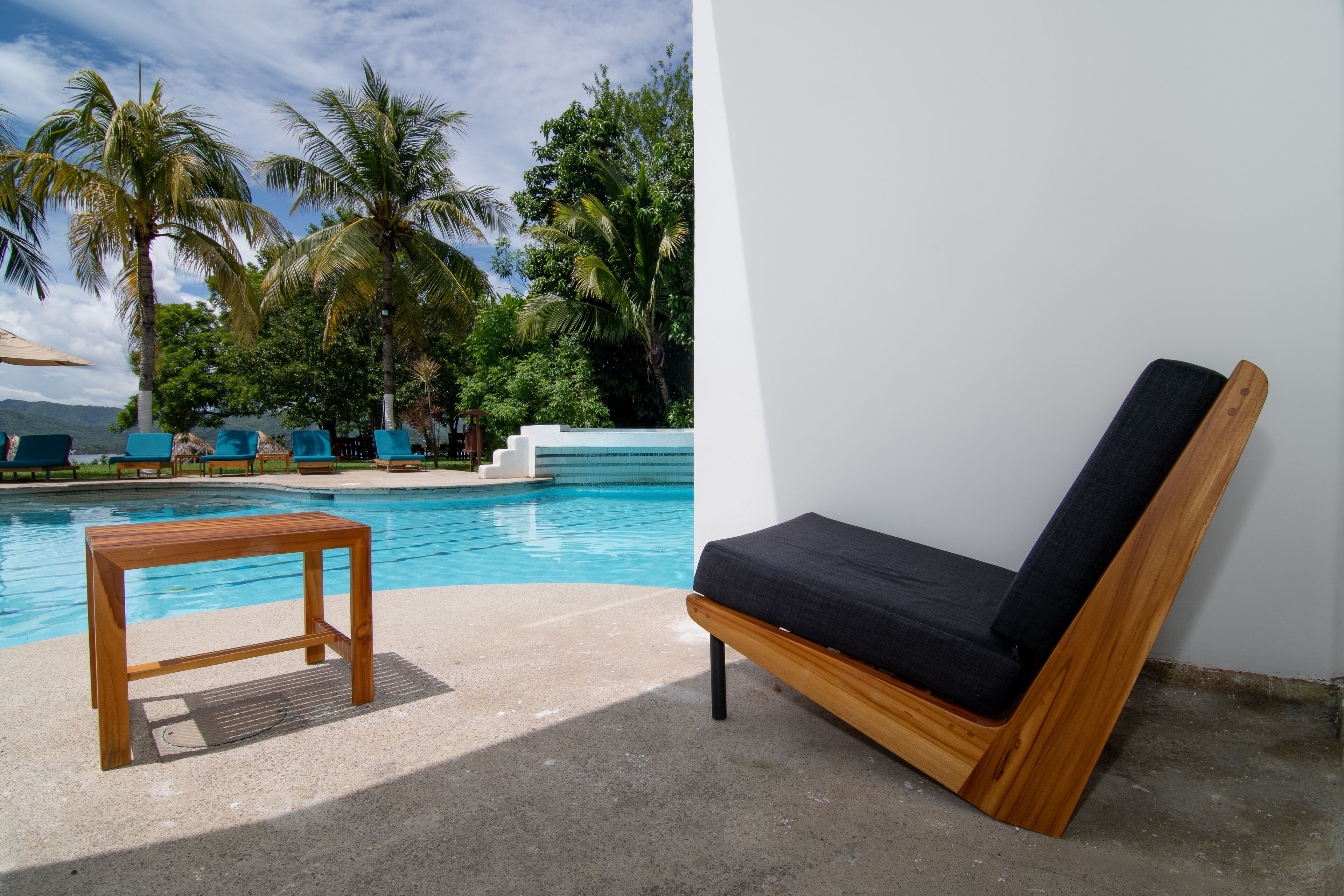 A poolside area with a wooden table and a wooden lounge chair.