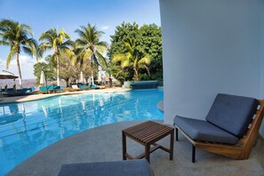 A pool area with lounge chairs and a wooden table, surrounded by palm trees and a clear sky. - Dunama Ocean View Hotel (Cabo Velas)