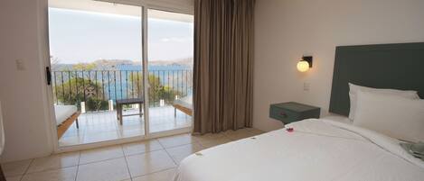 Une chambre d’hôtel avec un lit, une table de chevet, un banc et une vue sur la mer, accessible par une porte coulissante.