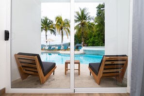 Quarto com porta de vidro que dá para uma área de piscina com espreguiçadeiras e uma mesa pequena.