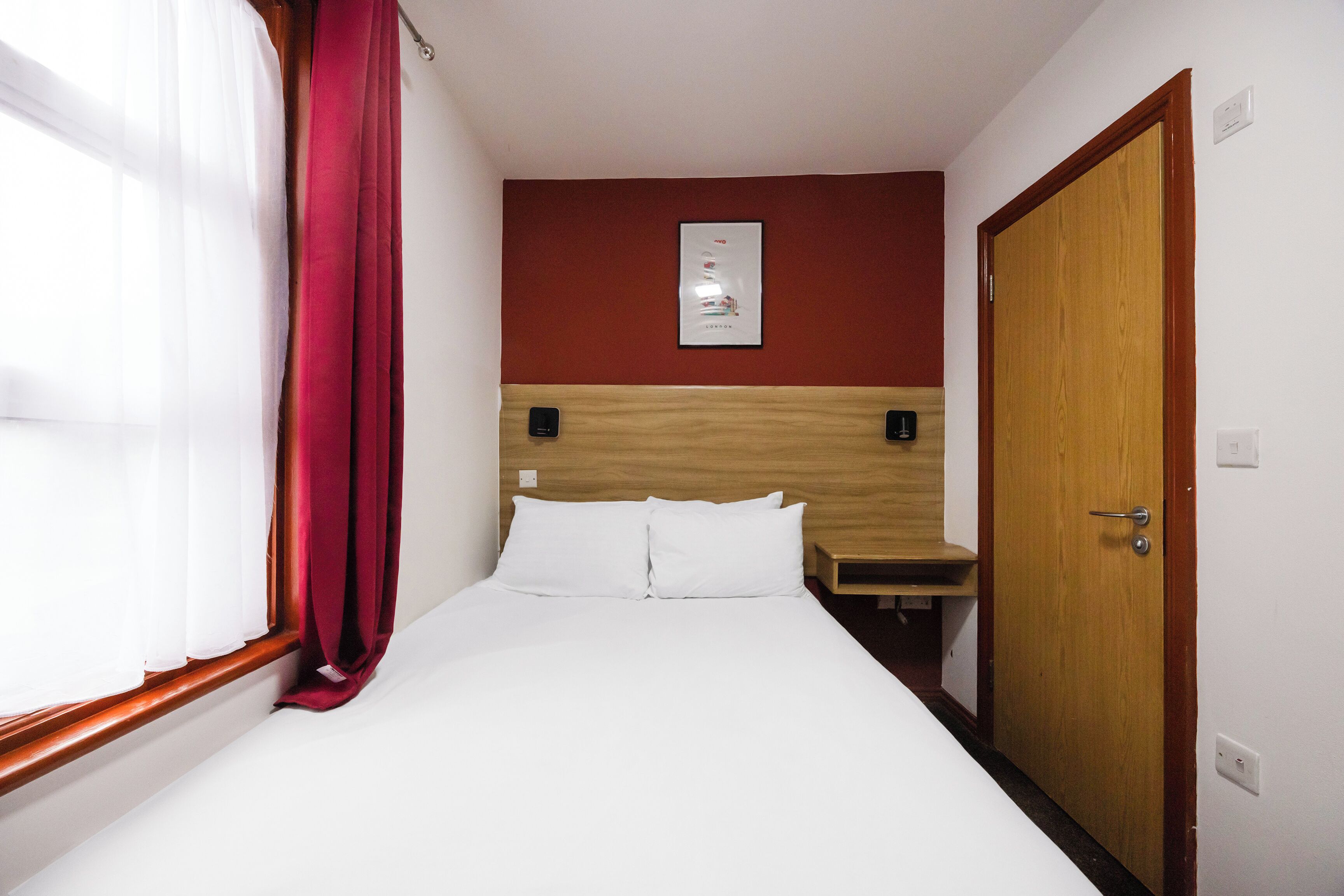 A hotel room with a bed, a wooden headboard, a small table, and a door.