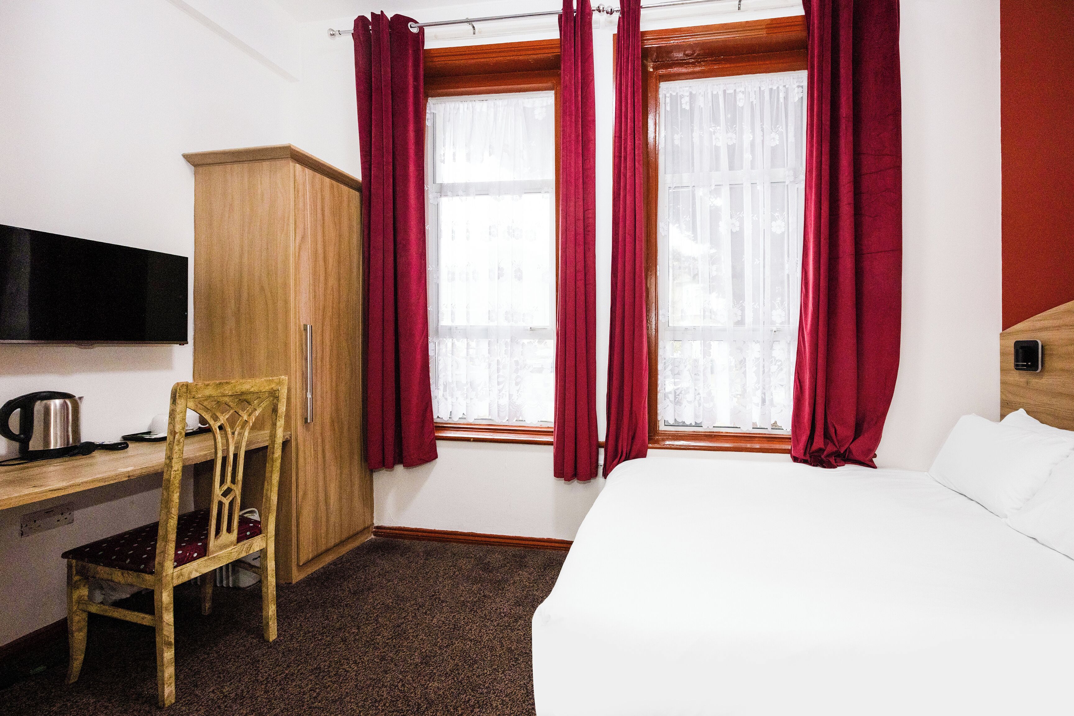 A hotel room with a wooden desk, a chair, a bed, and a TV mounted on the wall.