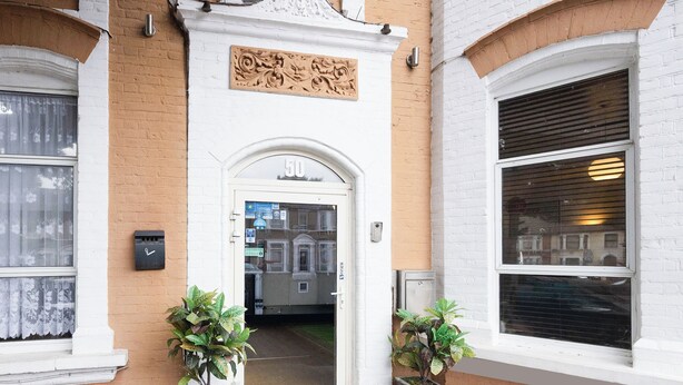 A building entrance with a white door marked "50", two potted plants, and a brick wall. - Arinza Hotel, London Ilford (Ilford)