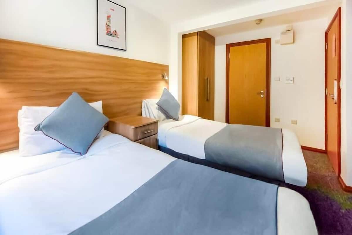Une chambre d’hôtel avec deux lits, une tête de lit en bois, une table de chevet et une porte donnant sur une autre pièce.