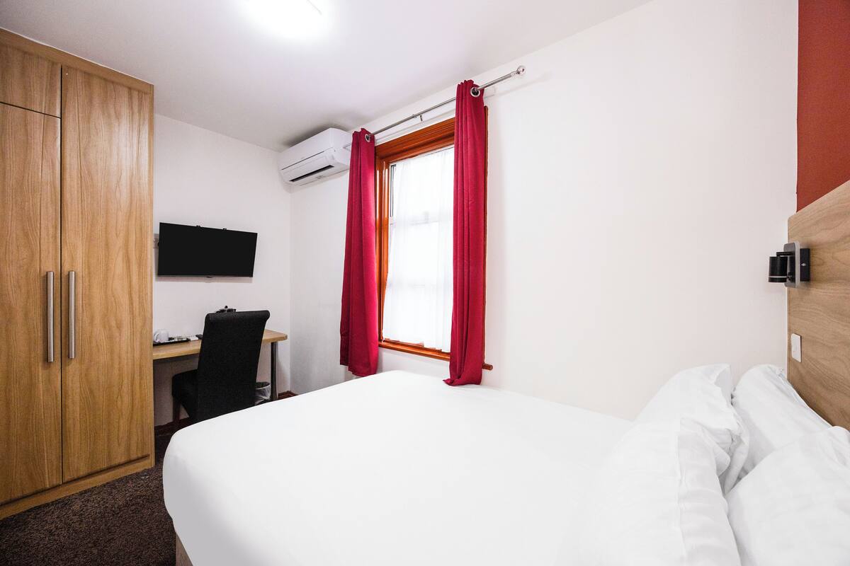 Une chambre d’hôtel comprenant un lit, un bureau avec une chaise, une télévision et une armoire.
