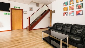 A lobby with a staircase, a black leather couch, a small table, and framed pictures on the wall. - Arinza Hotel, London Ilford (Ilford)