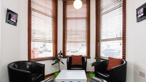 A modern living room with a white coffee table, black leather chairs, and large windows with blinds. - Arinza Hotel, London Ilford (Ilford)