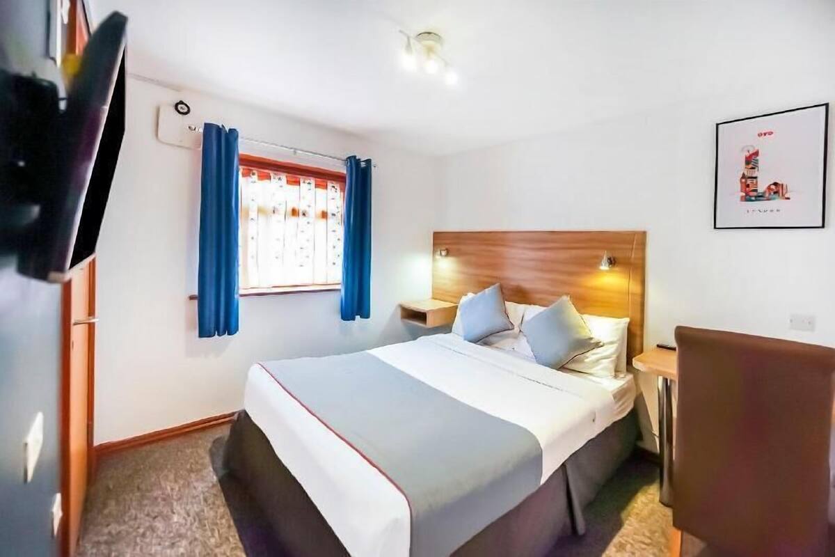 Une chambre d’hôtel comprenant un lit, des tables de chevet, une chaise, une fenêtre avec des rideaux et un luminaire fixé au mur.
