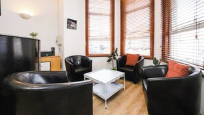 A modern living room with black leather sofas, a white coffee table, and wooden blinds on the windows. - Arinza Hotel, London Ilford (Ilford)