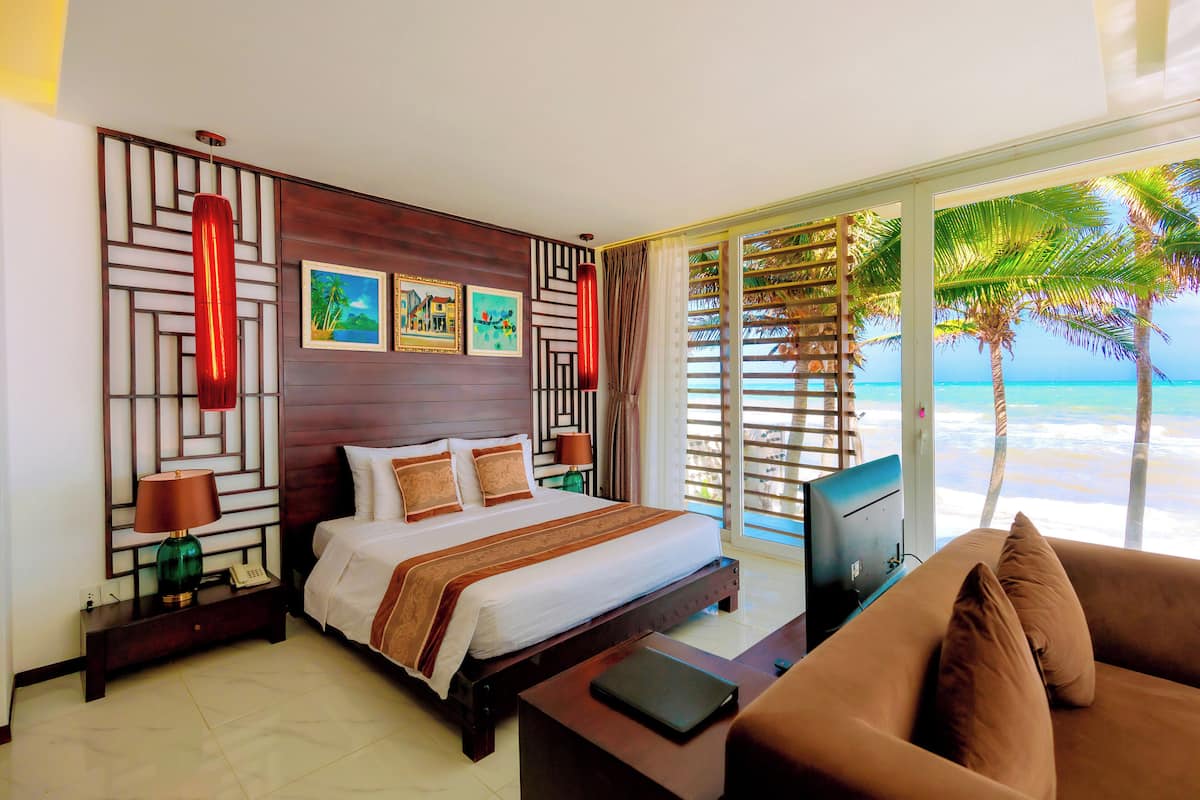 A hotel room with a bed, a TV, a sofa, and a view of the beach.