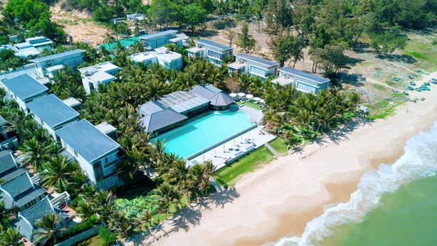 Vista aérea de un resort con varias construcciones, una piscina central y una playa.