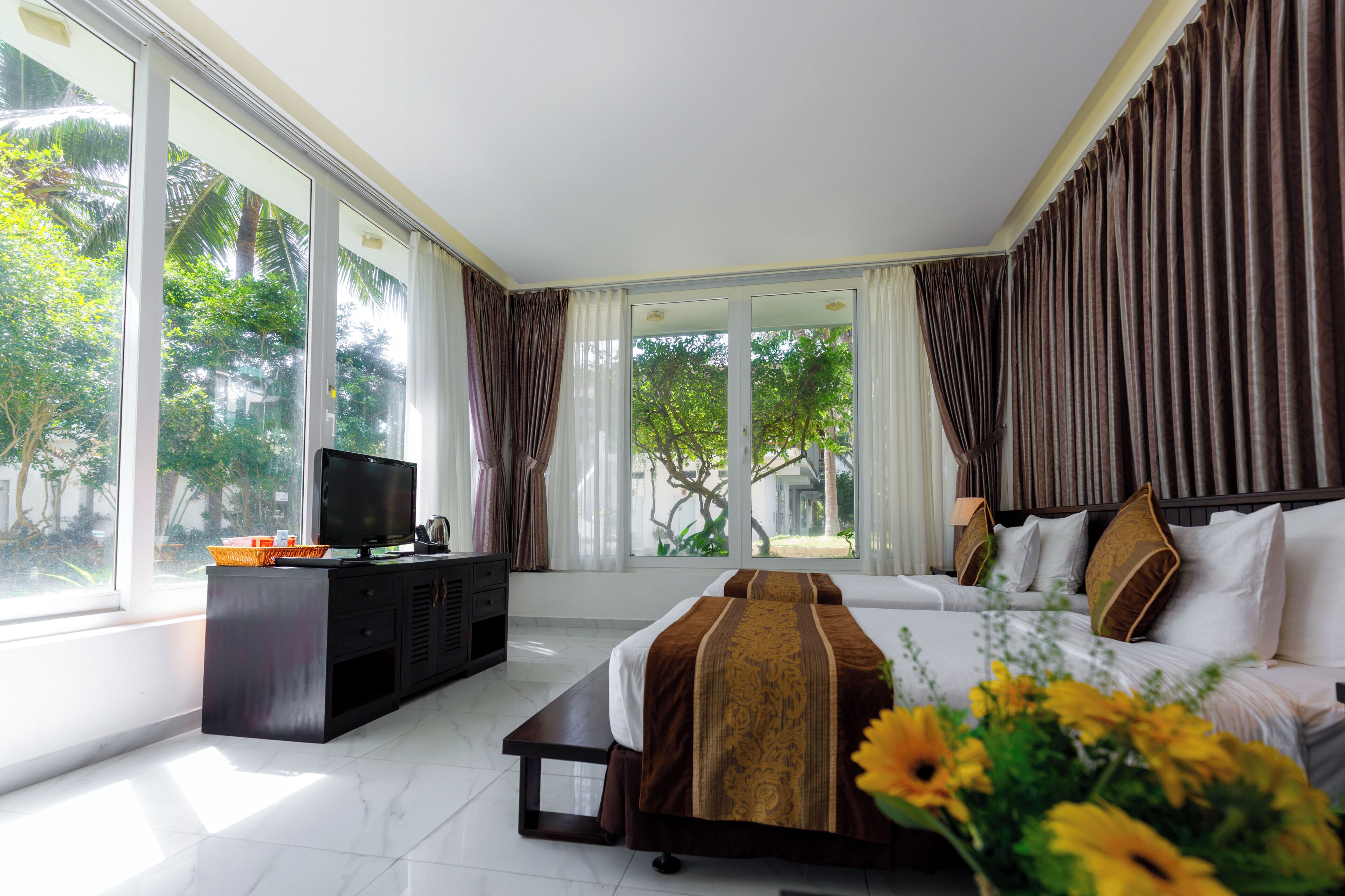 A hotel room with a bed, a TV, a desk, and large windows.