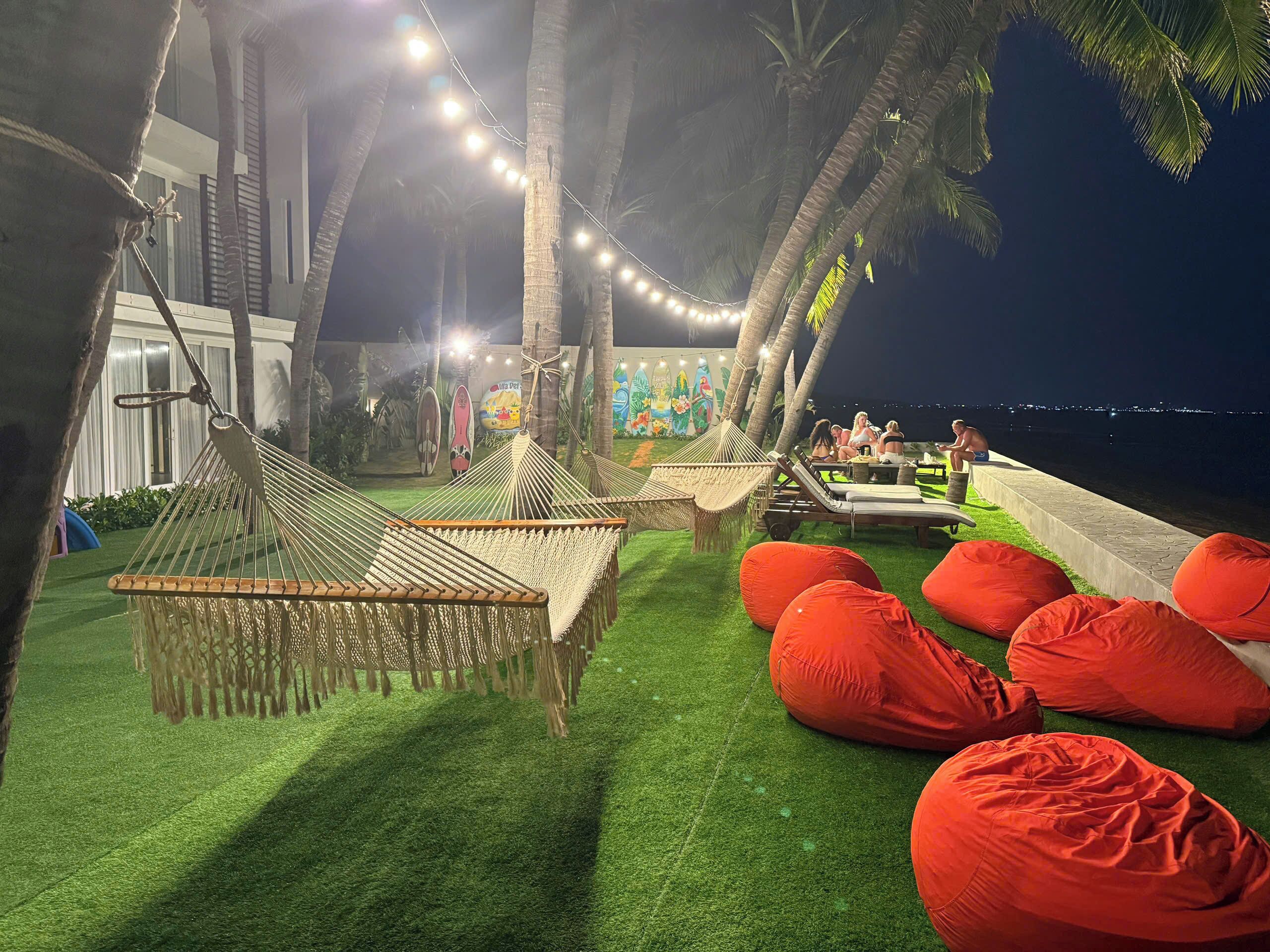 A nighttime outdoor seating area with hammocks and bean bags, palm trees, and a mural in the background.