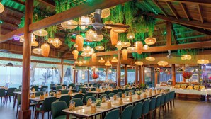 Un restaurante espacioso con techos altos, lámparas de mimbre colgantes y vistas al océano.