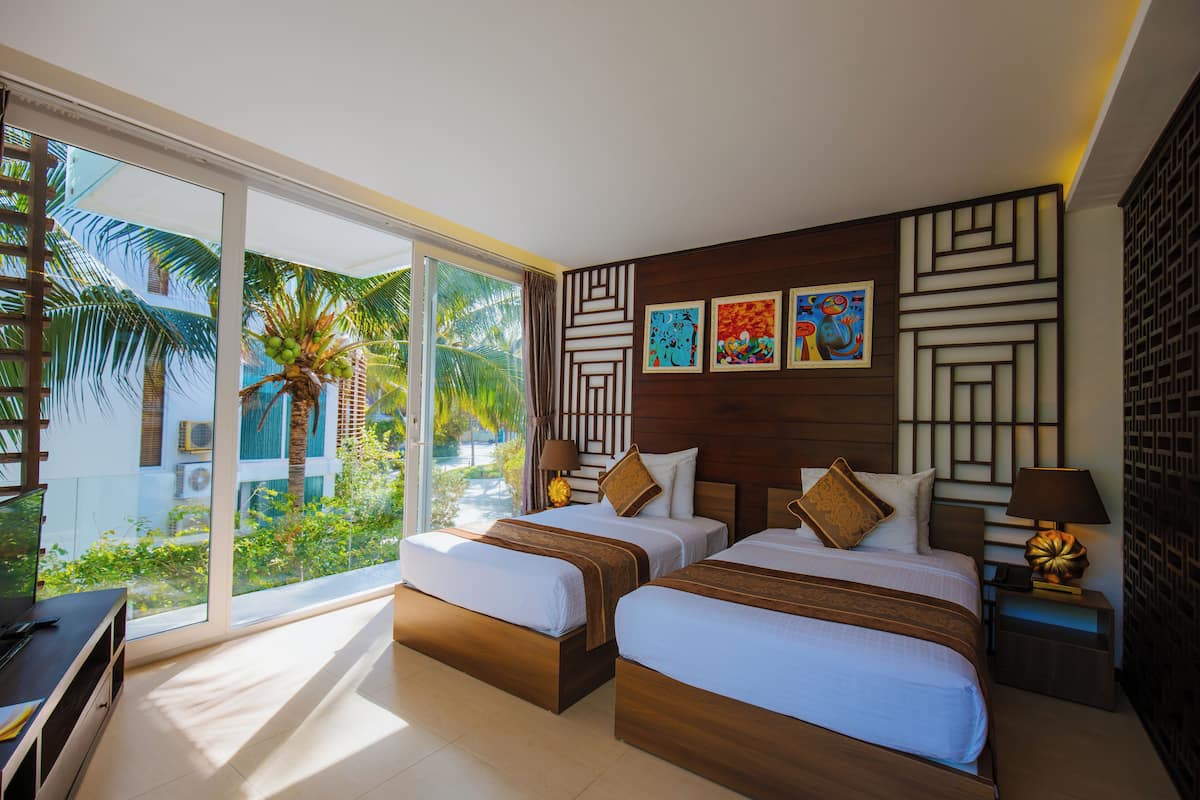 A hotel room with two beds, a balcony with a view of palm trees, and artwork on the wall.