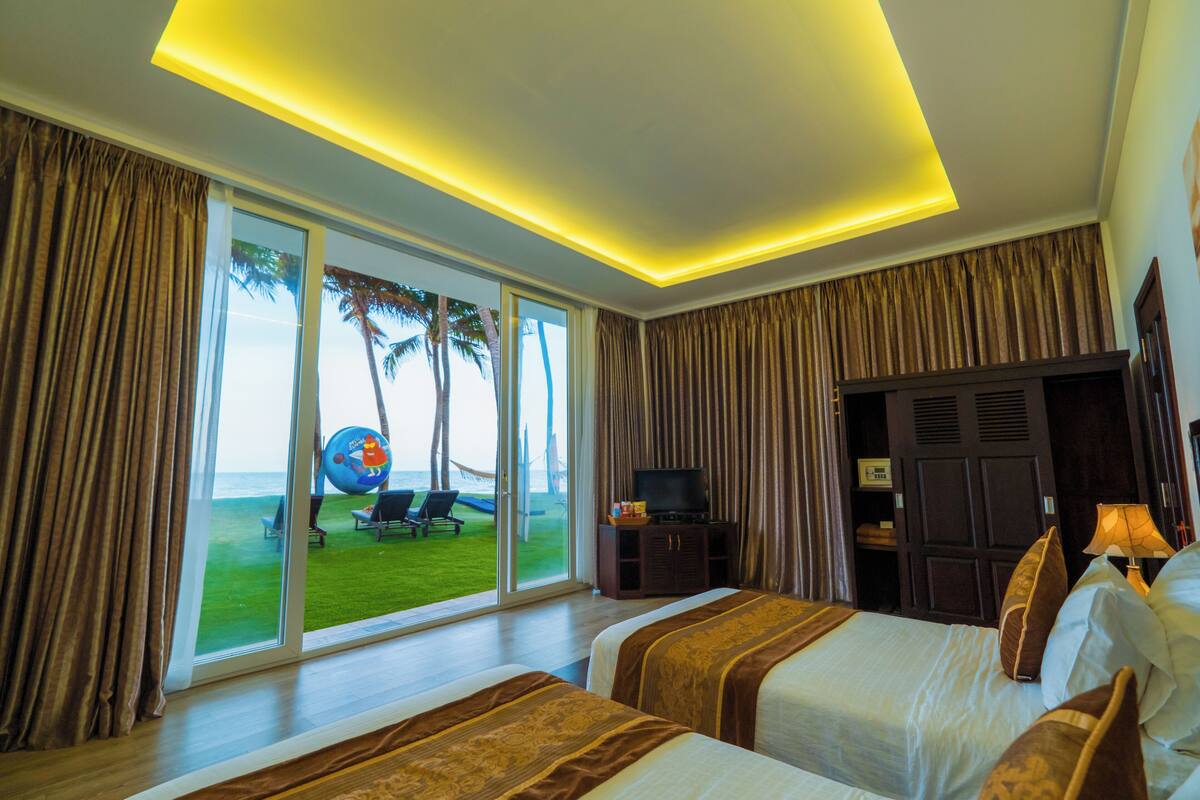 A hotel room with two beds, a TV, and a view of the beach.