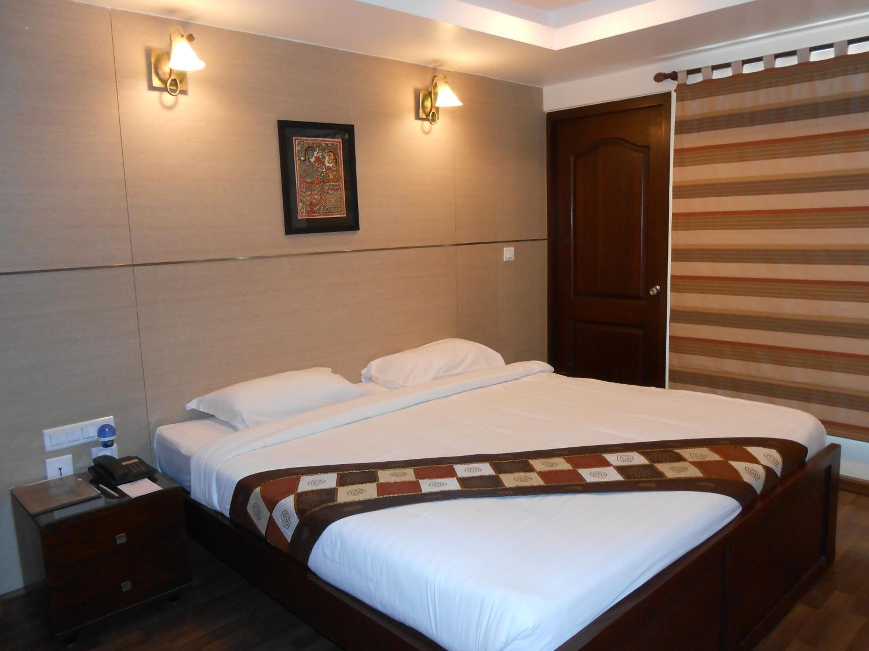 Una habitación de hotel con cama, mesitas de noche, teléfono y un cuadro en la pared.