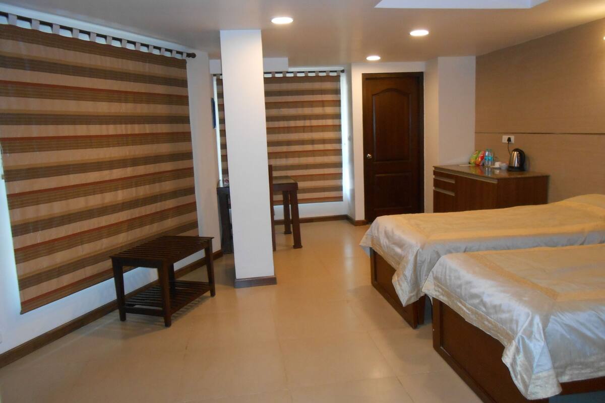 A hotel room with two beds, a wooden desk, a chair, and a wardrobe.