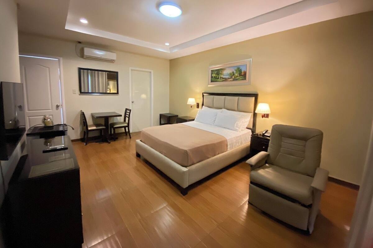 Una habitación de hotel con cama, escritorio, silla, televisor y un cuadro en la pared.