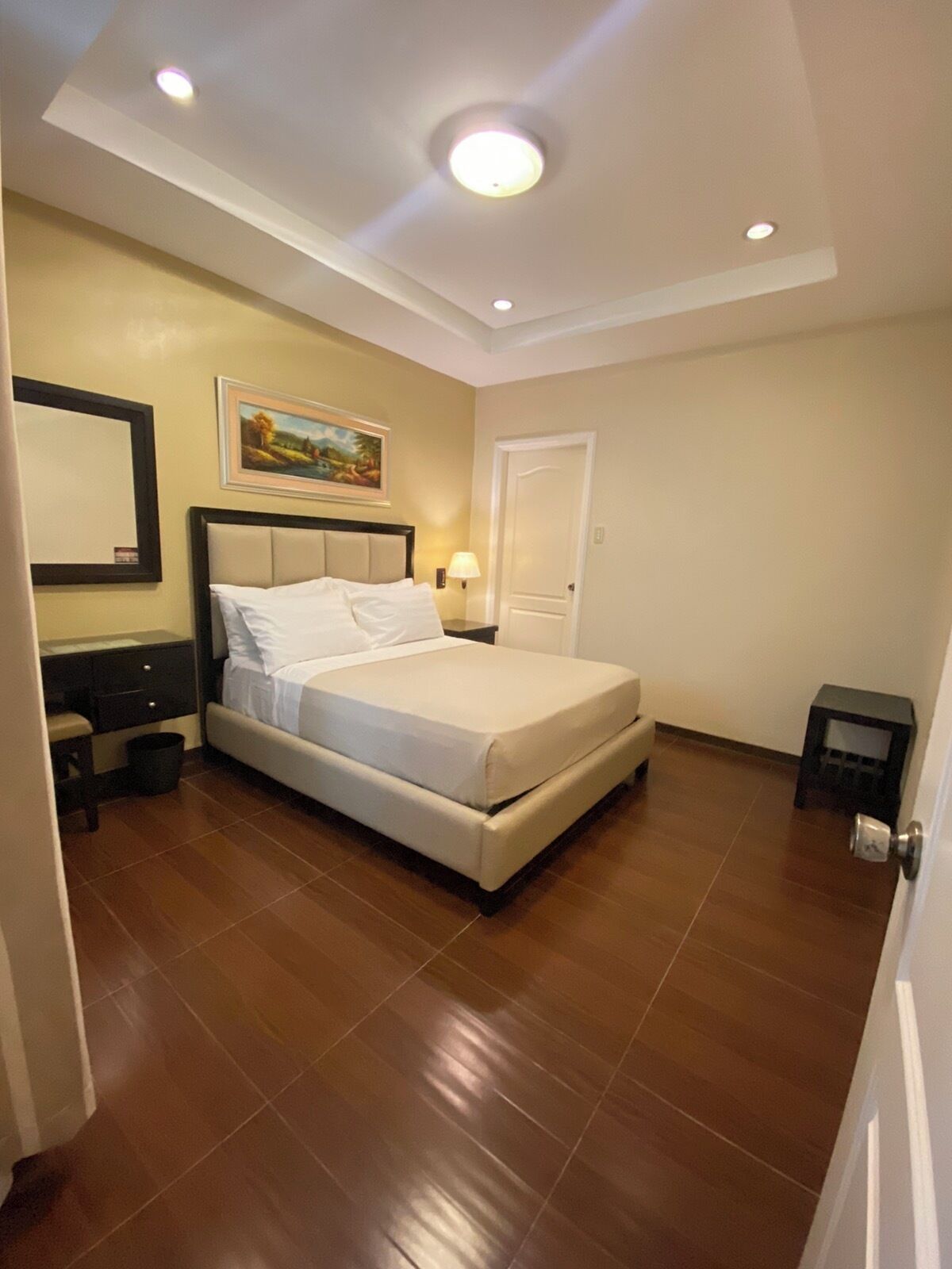 A bedroom with a bed, a nightstand, a lamp, a door, and a painting on the wall.