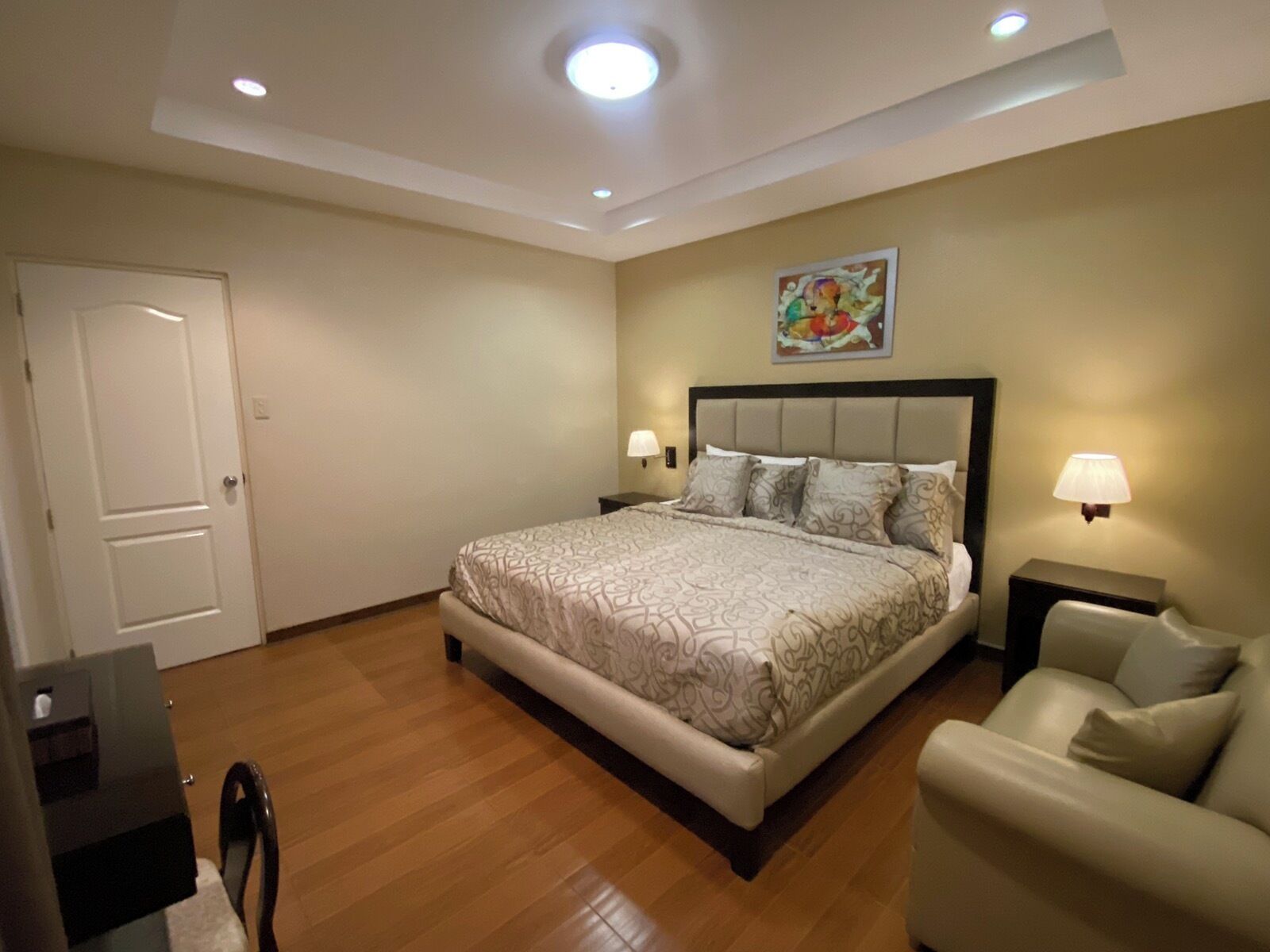 A bedroom with a large bed, two bedside tables with lamps, a chair, and a door.