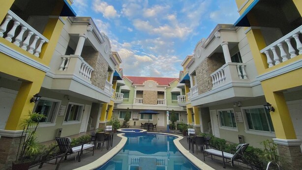A hotel with a central swimming pool surrounded by balconies and outdoor seating areas. - Prism Hotel (Angeles City)