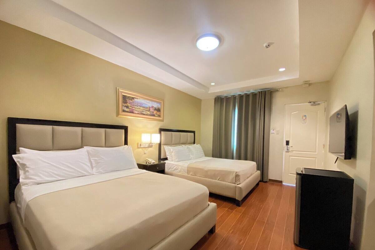 Habitación de hotel con dos camas, un cuadro en la pared, un televisor y una puerta.