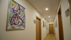 A hallway with a large abstract painting on the left, wooden doors, and framed pictures on the walls. - Hotel Piazza Marconi (Cassino)