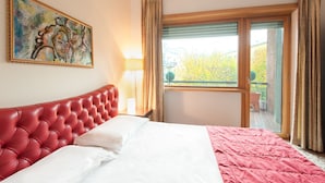 A hotel room with a red tufted headboard, a large window with a view of trees, and a painting on the wall. - Hotel Piazza Marconi (Cassino)