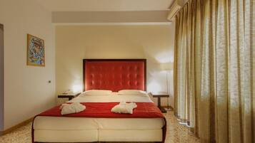 A hotel room with a red tufted headboard, a large bed with white linens, two bedside tables, and a painting on the wall.