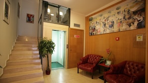 A hotel lobby with a staircase, wooden walls, a large mural, and two leather armchairs. - Hotel Piazza Marconi (Cassino)