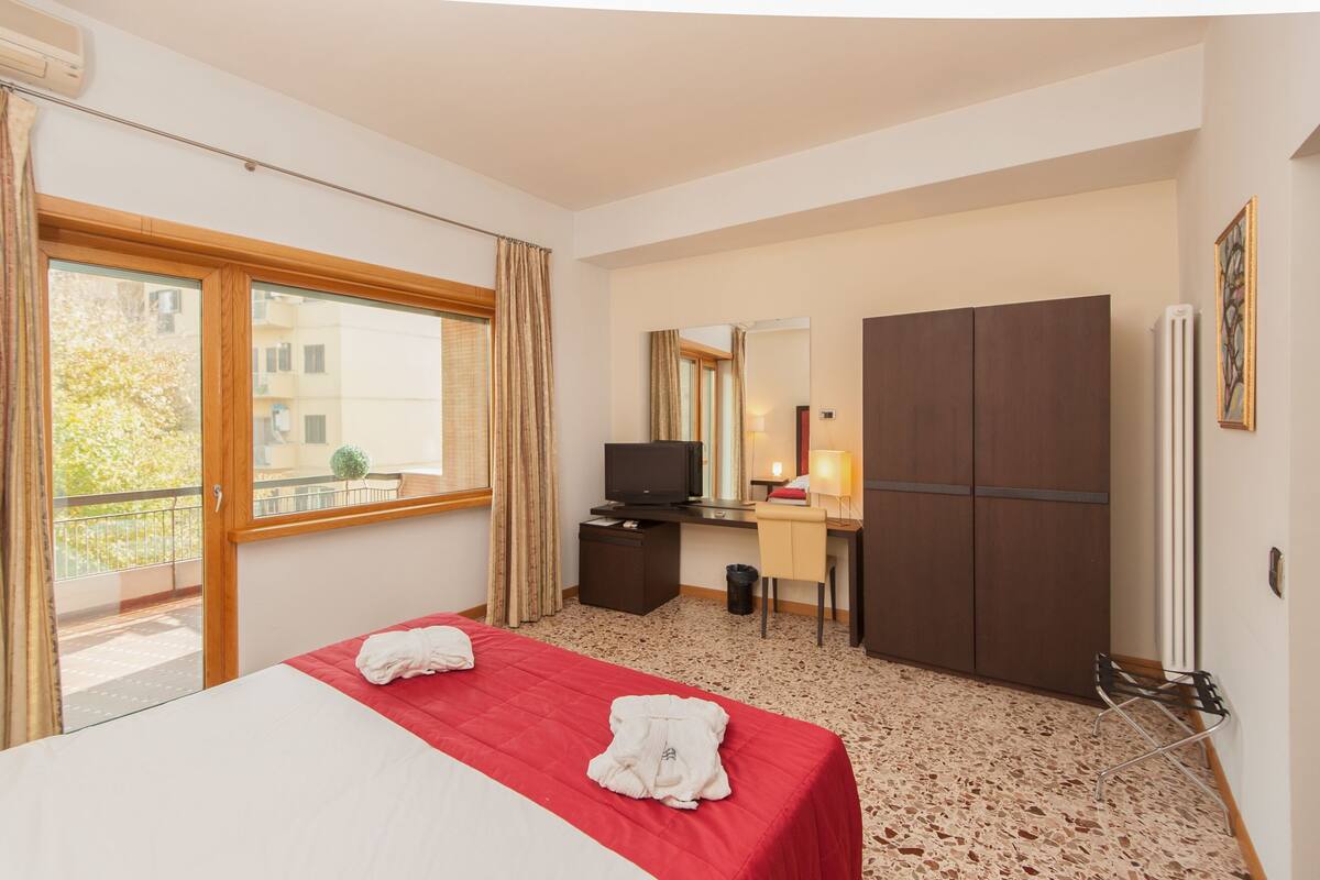 Ein Hotelzimmer mit Bett, Schreibtisch, Fernseher, Kleiderschrank und Balkon.