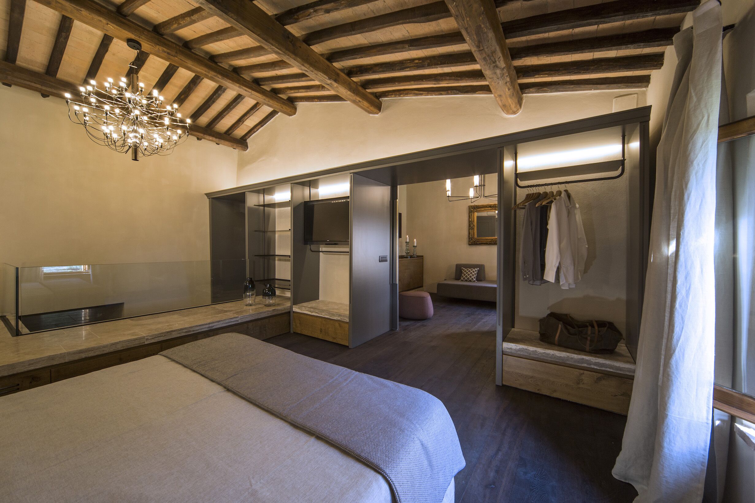 Une chambre moderne avec un grand lit, une coiffeuse avec un miroir et un dressing où les vêtements sont suspendus.