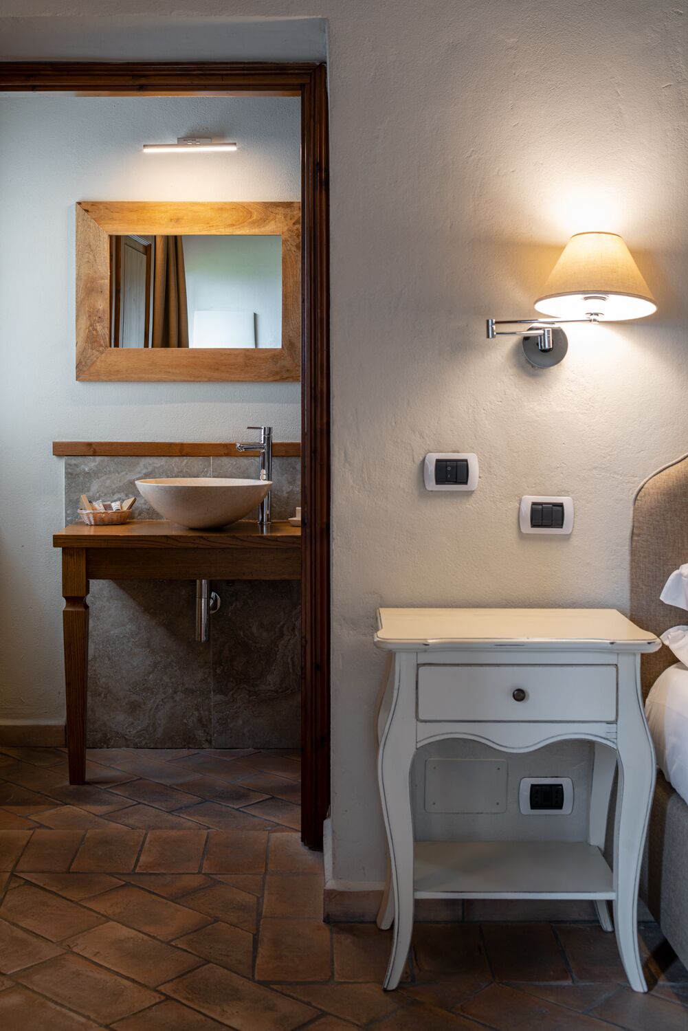 A bathroom with a wooden vanity, a large mirror, a wall-mounted light, and a small cabinet.