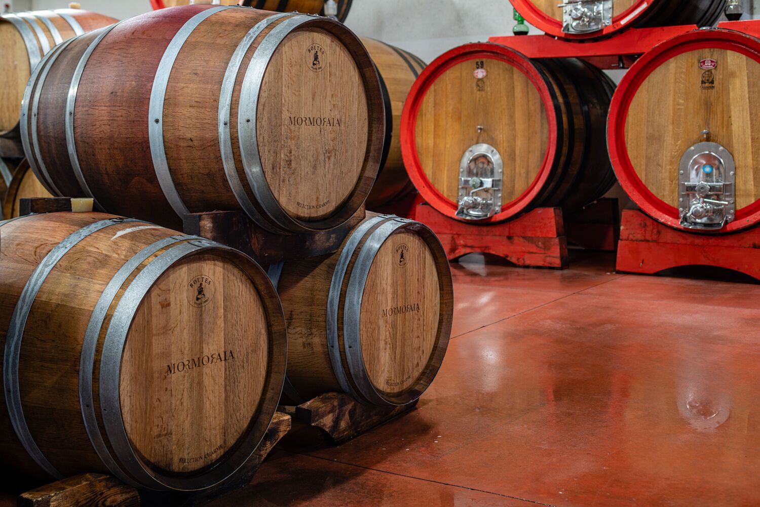 Wooden wine barrels with metal bands and a red barrel pump in a warehouse.