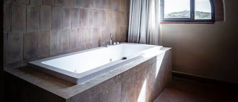 A modern bathroom with a freestanding bathtub, stone walls, and a view through a window.