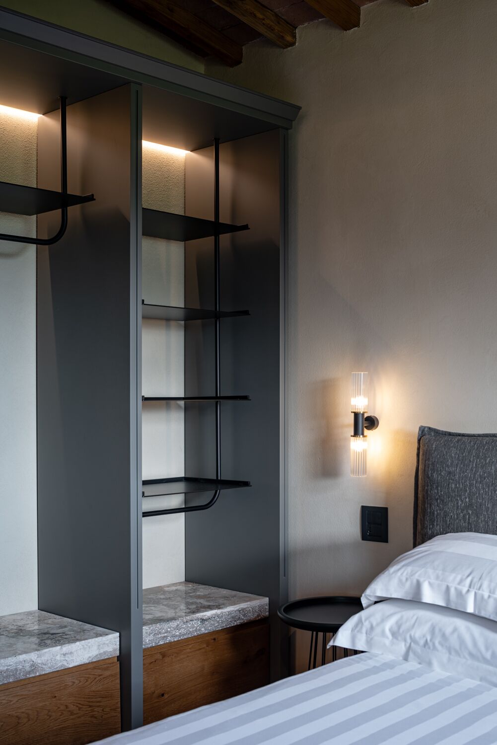 A bedroom with a bed, a nightstand, a wall-mounted light, and a built-in wardrobe with shelves.