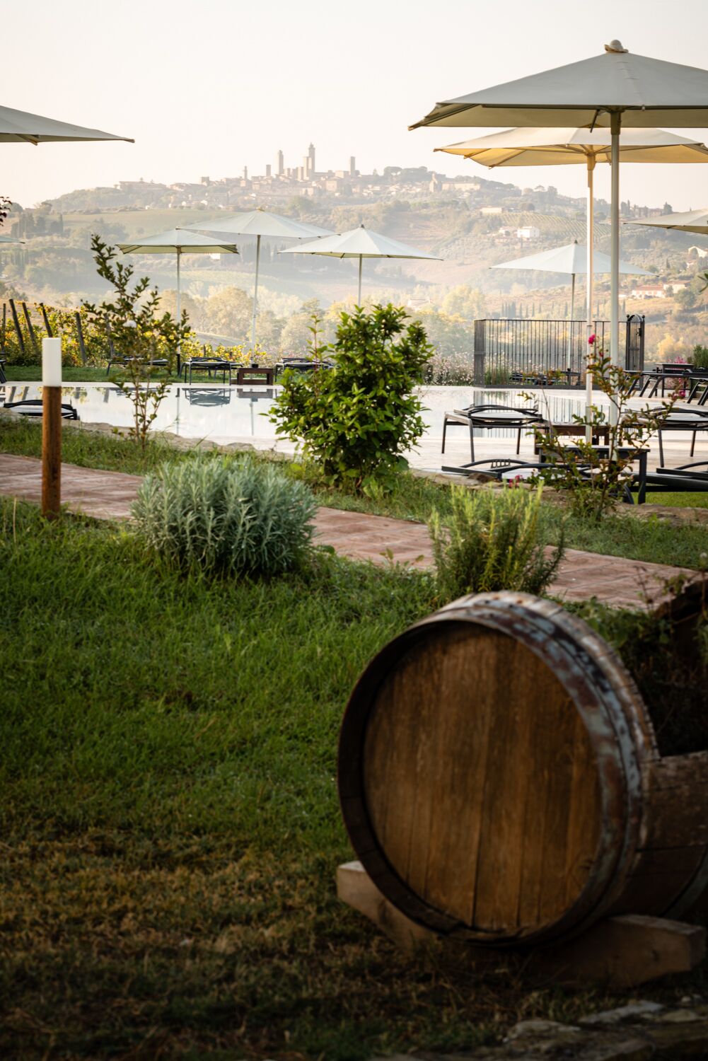 A serene outdoor seating area with tables and chairs under umbrellas, overlooking a body of water and a distant cityscape.