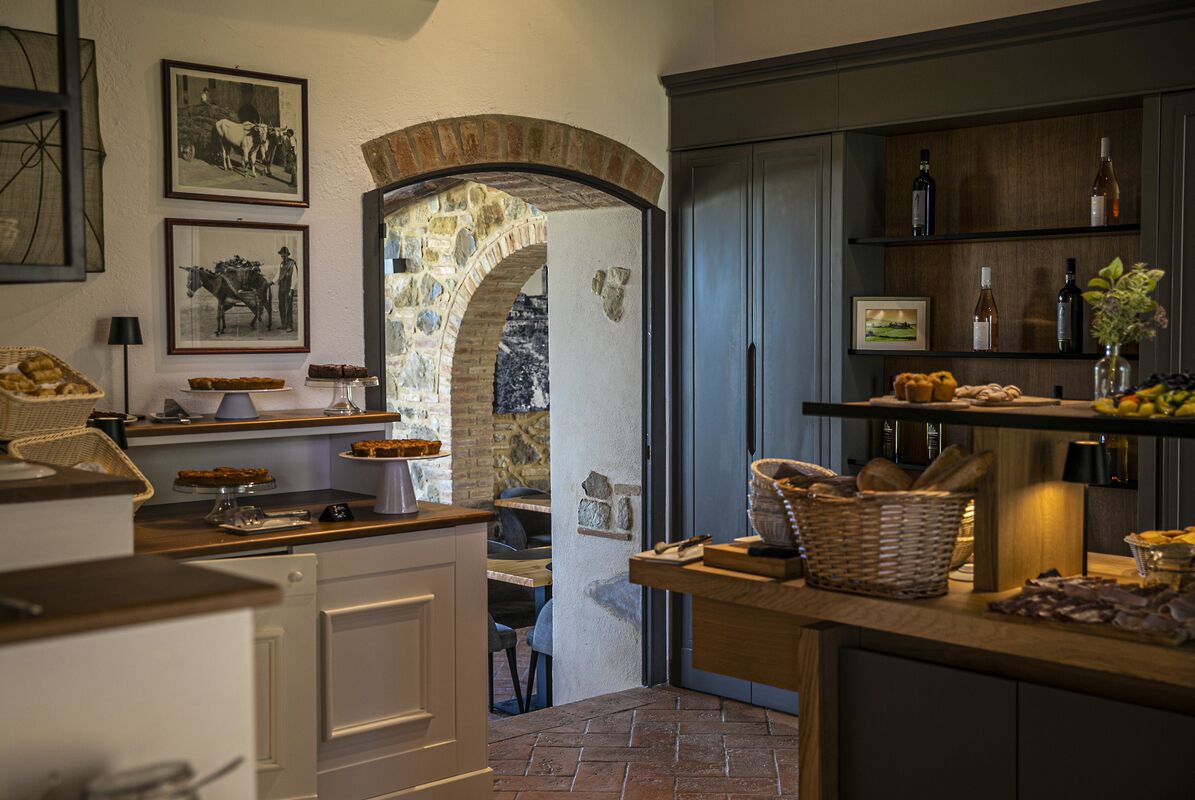 A kitchen with a stone archway, wooden shelves with bottles, and a basket of bread.