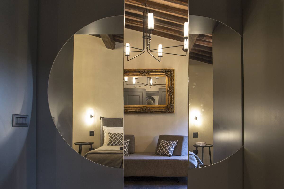 A modern interior with a circular mirror reflecting a room with a bed, a painting, and a chandelier.