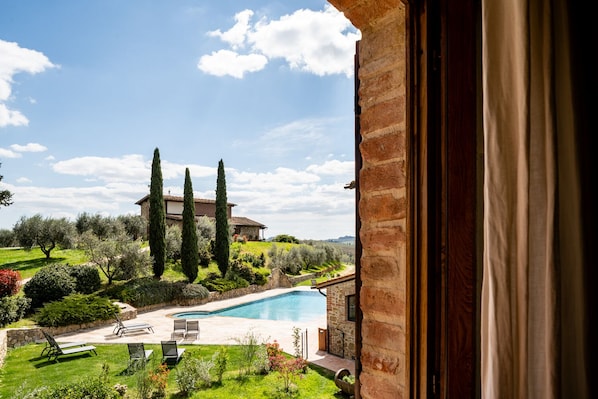A view of a swimming pool with lounge chairs, surrounded by greenery and tall trees, with a building in the background. - Mormoraia (San Gimignano)