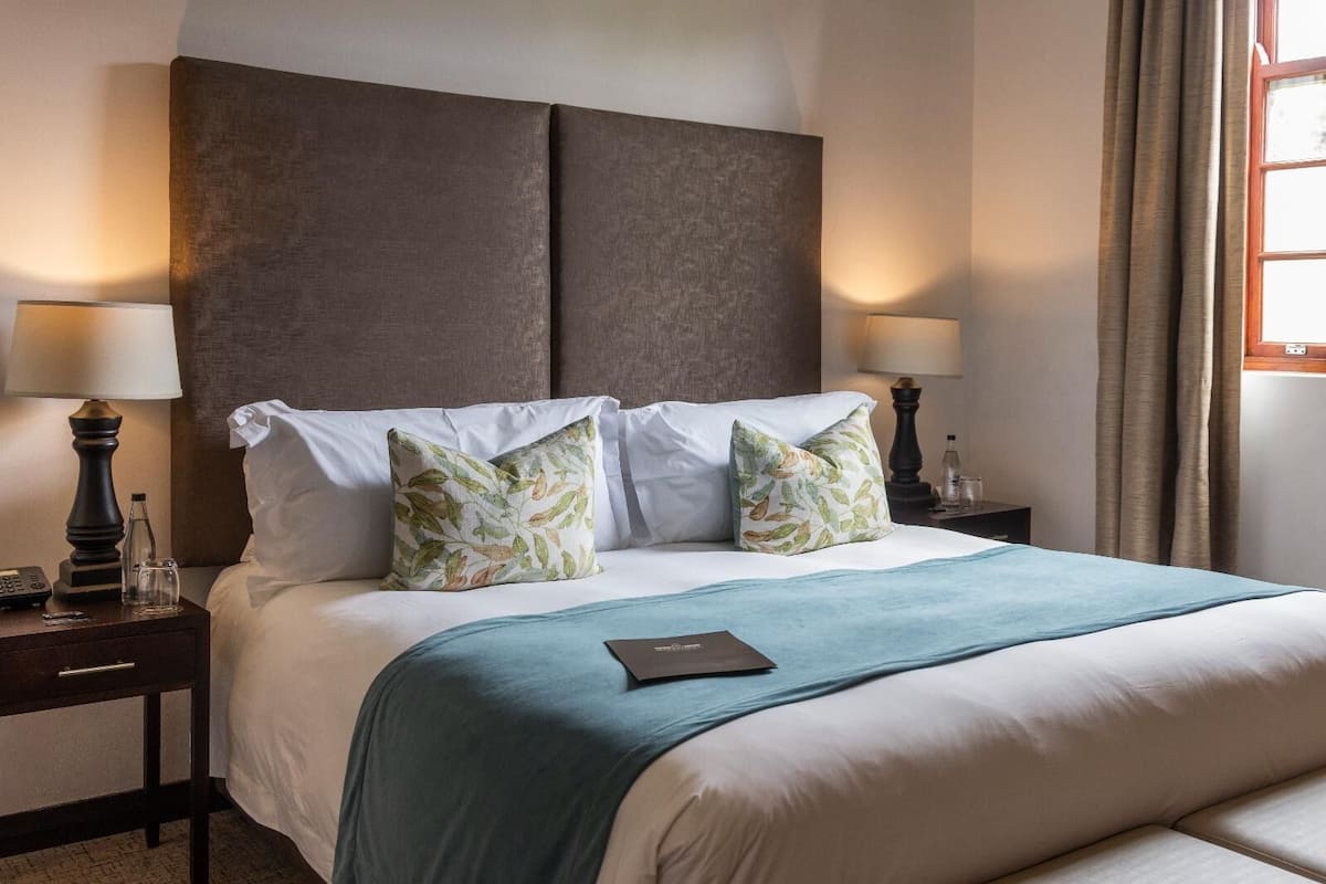 A neatly made bed with a blue bedspread, two white pillows, and a dark headboard. There are two bedside tables with lamps and a small bottle on one.